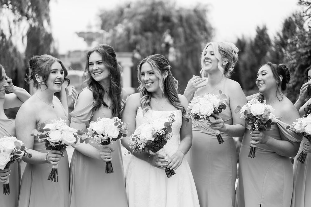 A row of wedding party members in gray dresses holding white bouquets share laughs together outdoors.