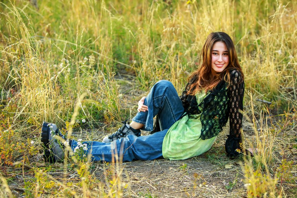 Person in blue denim and green top laying in golden grass field during sunset photoshoot.