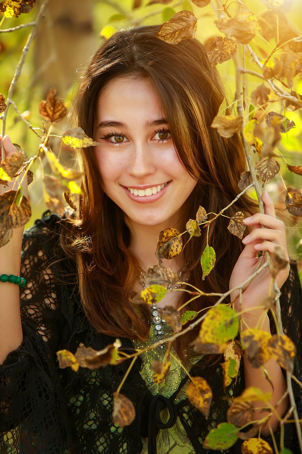 Someone poses outdoors in a black lace dress surrounded by autumn leaves and warm golden sunlight.