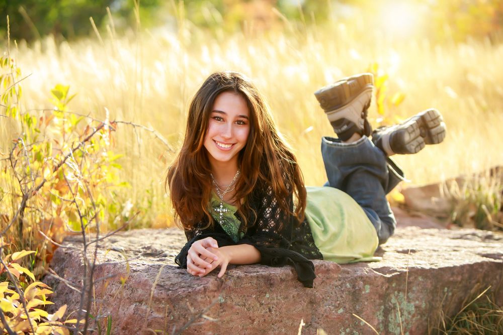 Person in green sweater lying on rustic log in autumn sunlit meadow with golden bokeh background.