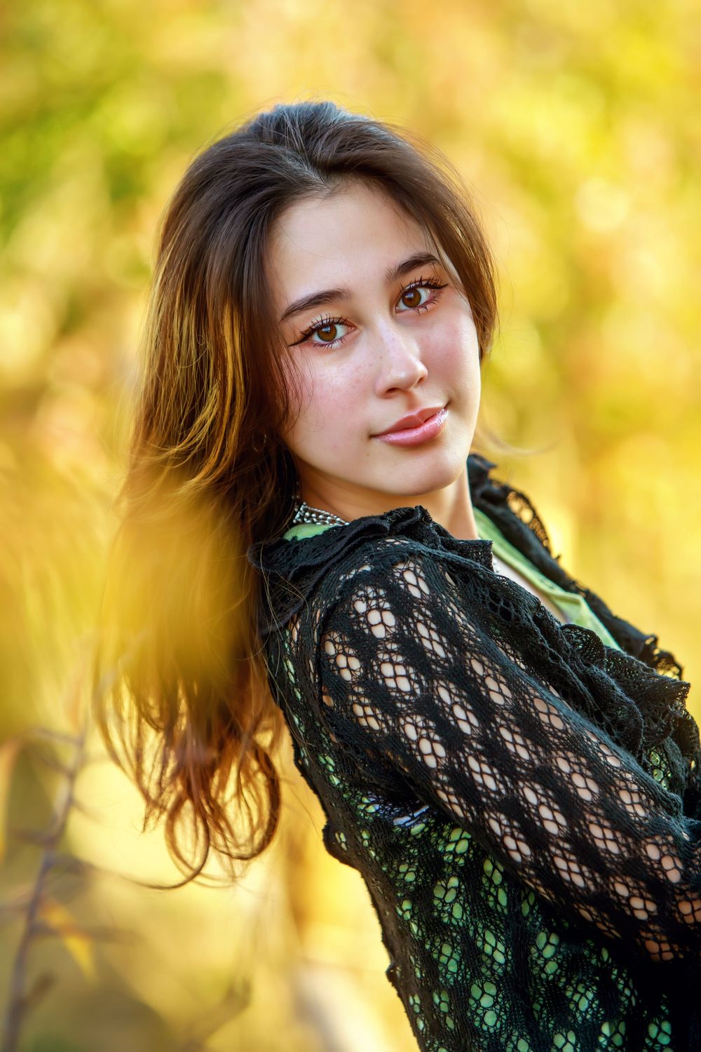 A person in a black lace top poses against a dreamy golden bokeh background creating an artistic portrait effect.