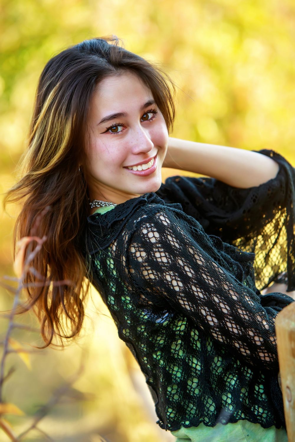 A person in a black lace top poses gracefully against a warm golden autumn background.