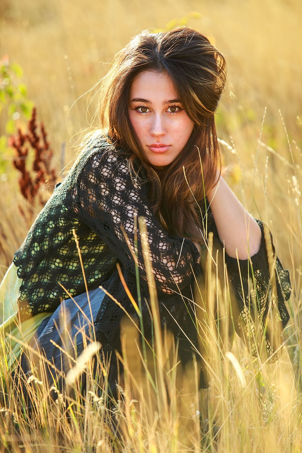 A person in a patterned sweater poses playfully in golden autumn wheat fields during sunset.