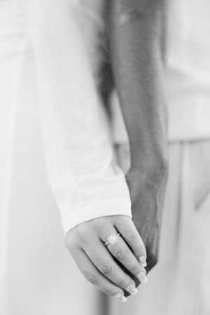 Black and white close-up of hands holding together, with an engagement ring prominently displayed.