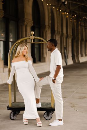 Sweet couple in all white outfits share romantic moments under vintage archways on cobblestone street.