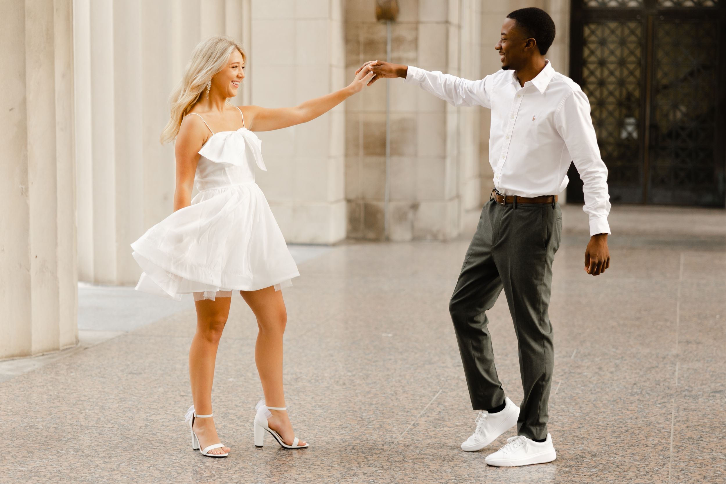 A couple in formal attire dance together outdoors, with the woman wearing a white dress and the man in a white shirt.