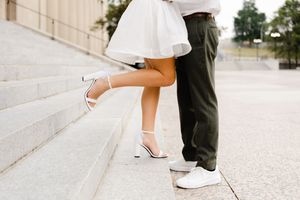 A couple on marble steps showing shoes and legs with the bride in white heels and groom in casual sneakers.