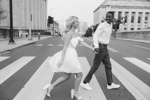 Two people joyfully dance across a city crosswalk wearing white clothing in a black and white photograph.