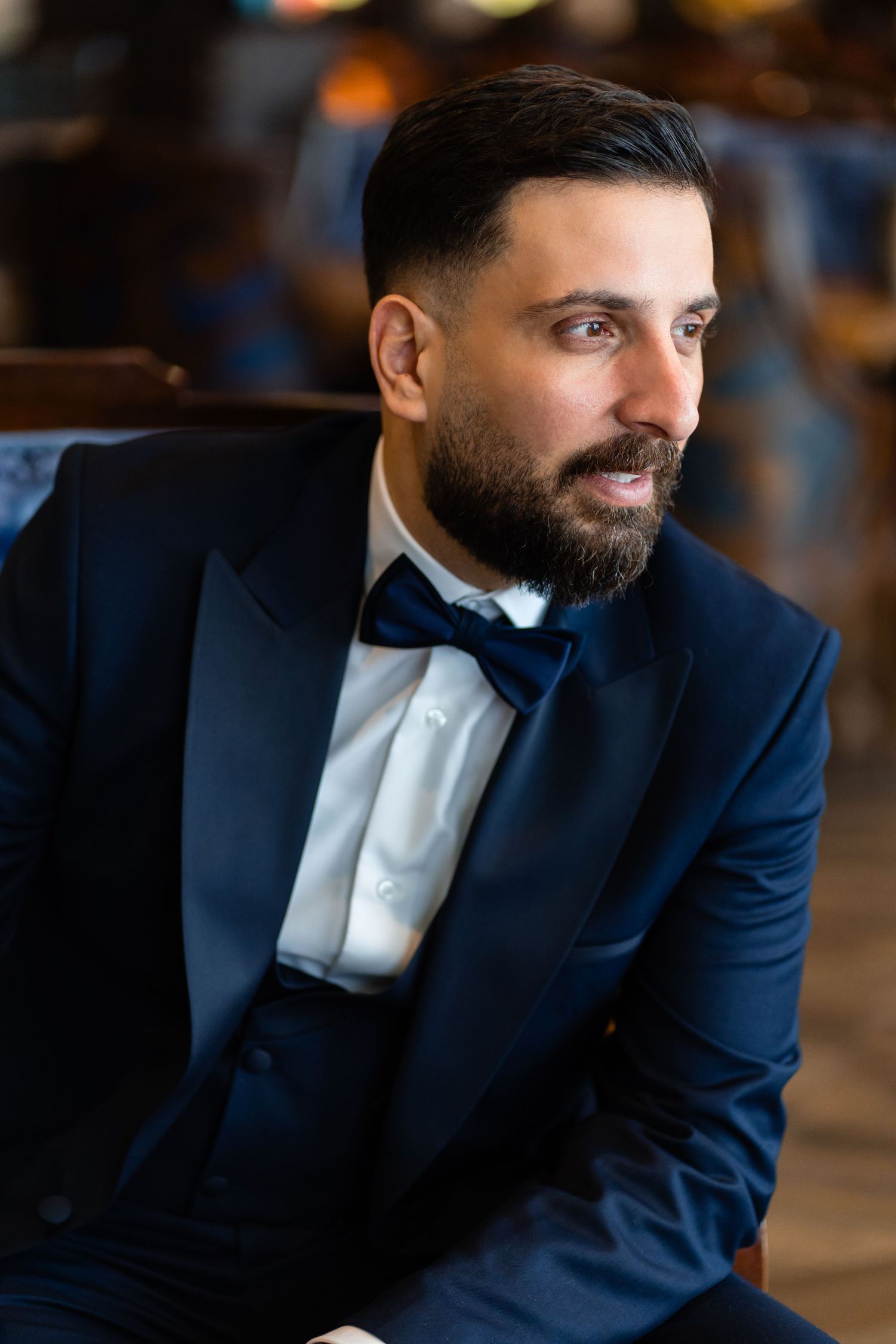Elegant portrait of someone in a navy blue tuxedo with bow tie sitting in formal attire.