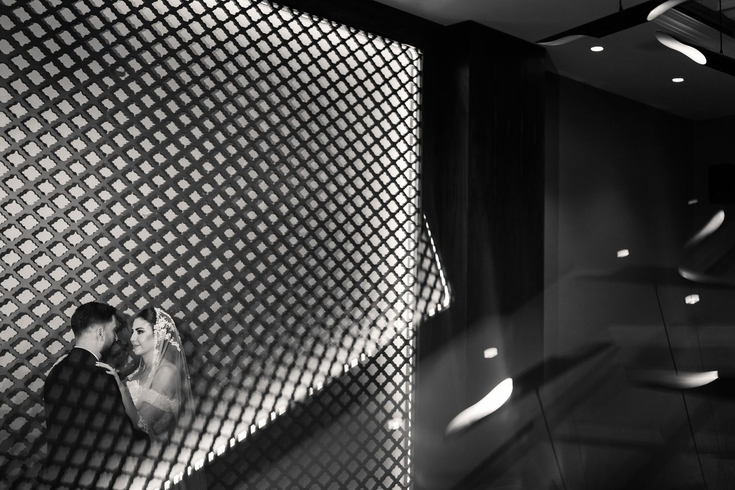 A dramatic black and white photograph of dancers performing against a geometric patterned wall with lighting effects.