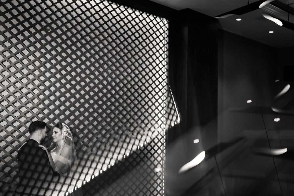 A dramatic black and white photograph of dancers performing against a geometric patterned wall with lighting effects.