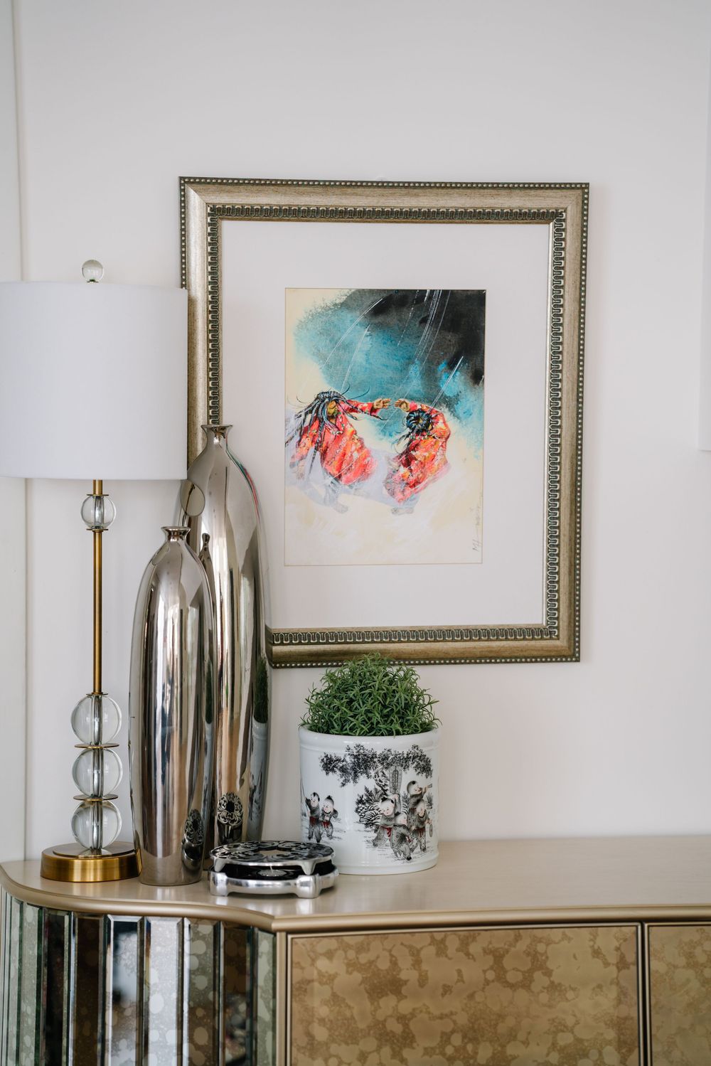 Modern mirrored cabinet with framed jellyfish art, silver lamps and decorative greenery.