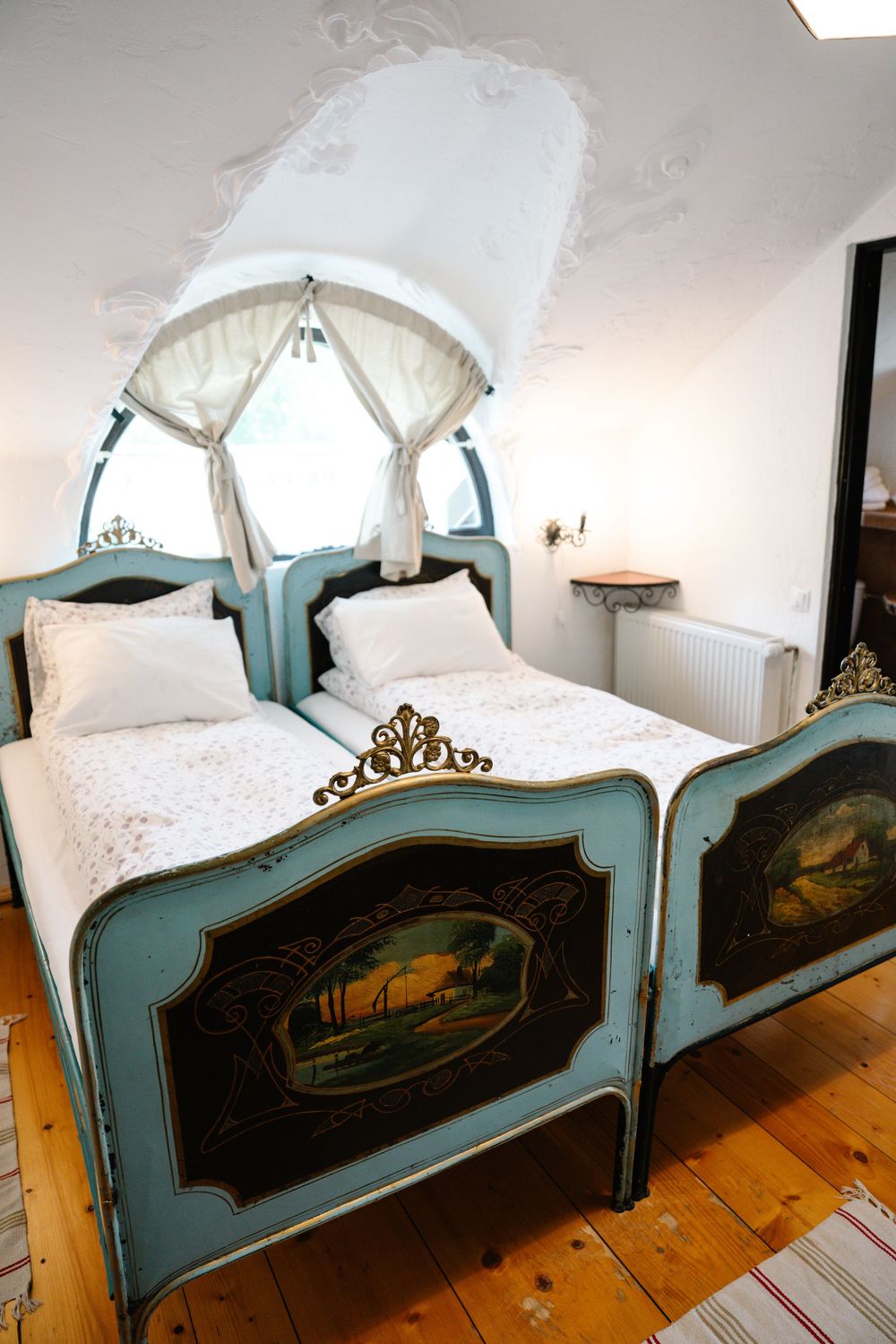 Ornate turquoise twin beds with painted landscape panels and white canopy.