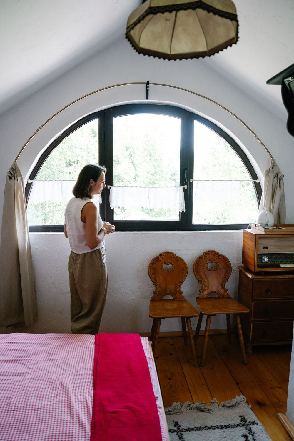 Cozy attic bedroom with arched window and vintage wooden chairs.