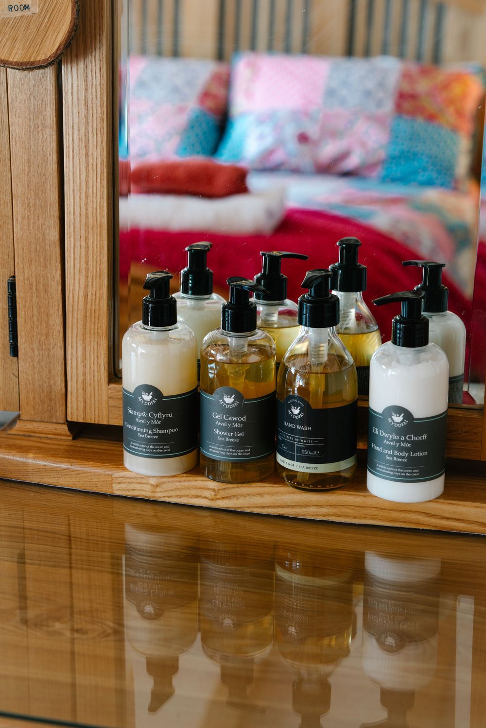 Collection of natural body care products displayed on a wooden surface with soft furnishings in background.