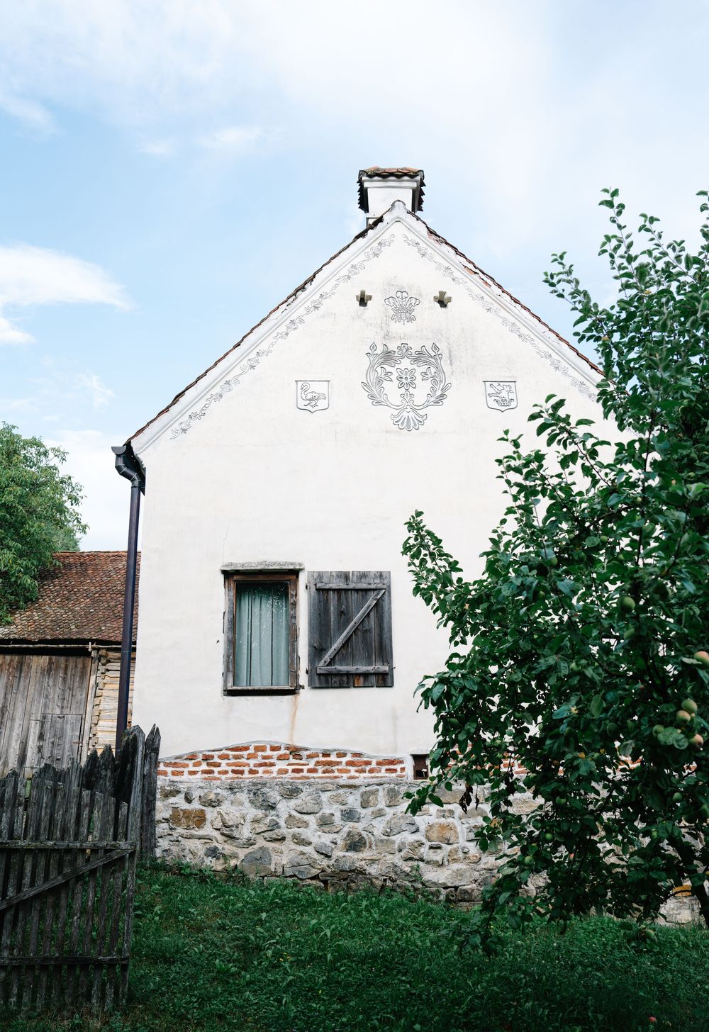 White farmhouse with stone foundation and wooden shutters against blue sky.