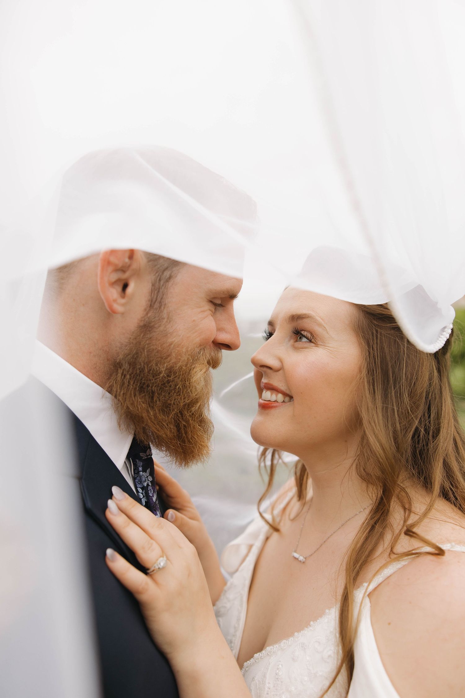 Close-up portrait of a romantic wedding couple gazing at each other under a white veil.