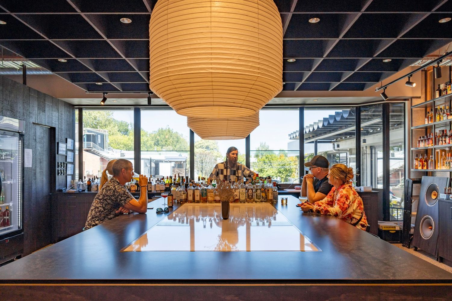 Bartender serves guests under large lanterns in a sleek, contemporary bar with warm light and wood textures.