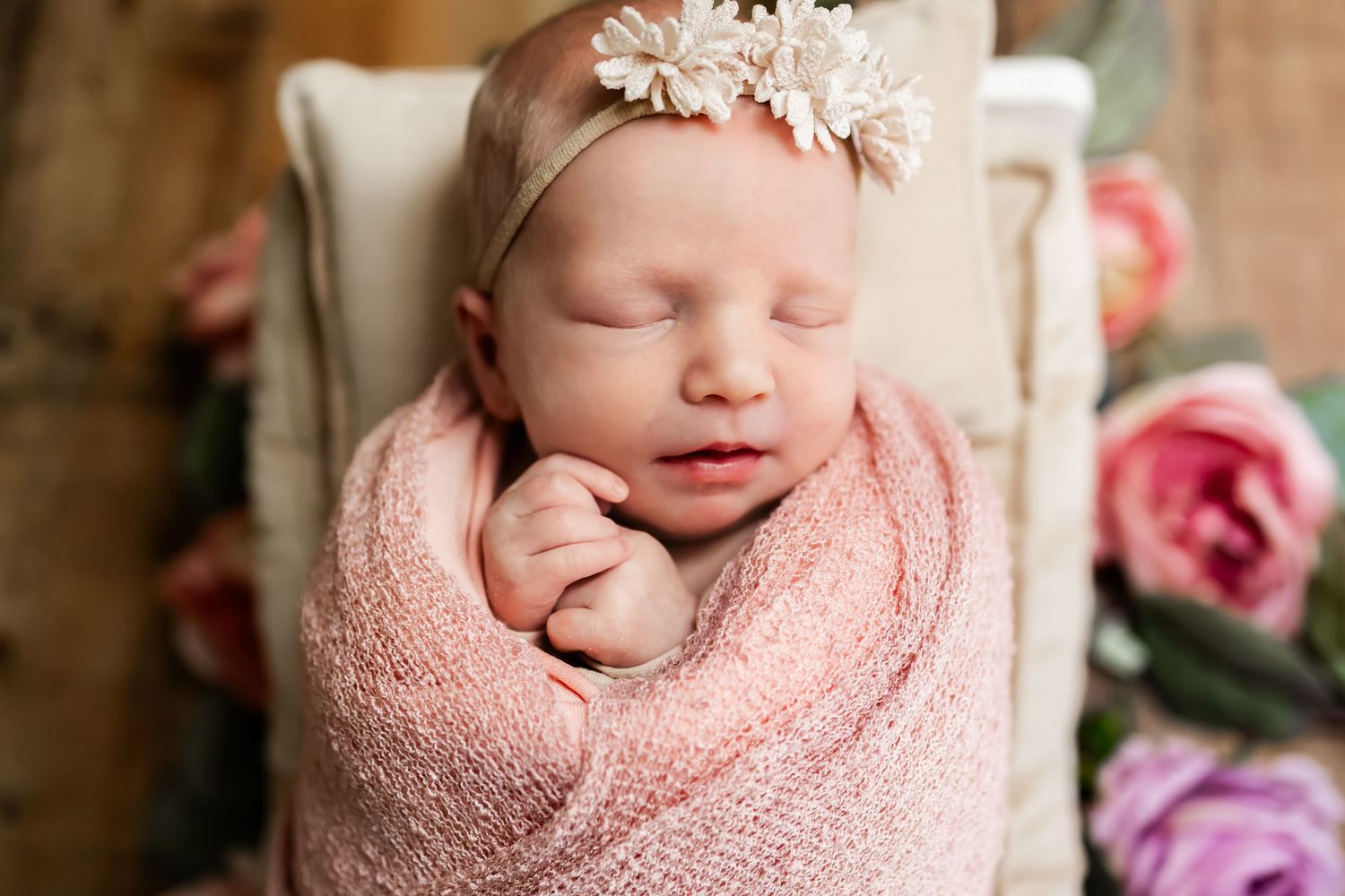 Newborn baby swaddled in soft pink blanket sleeping peacefully in white chair with roses nearby. newborn and maternity photographer in RVA