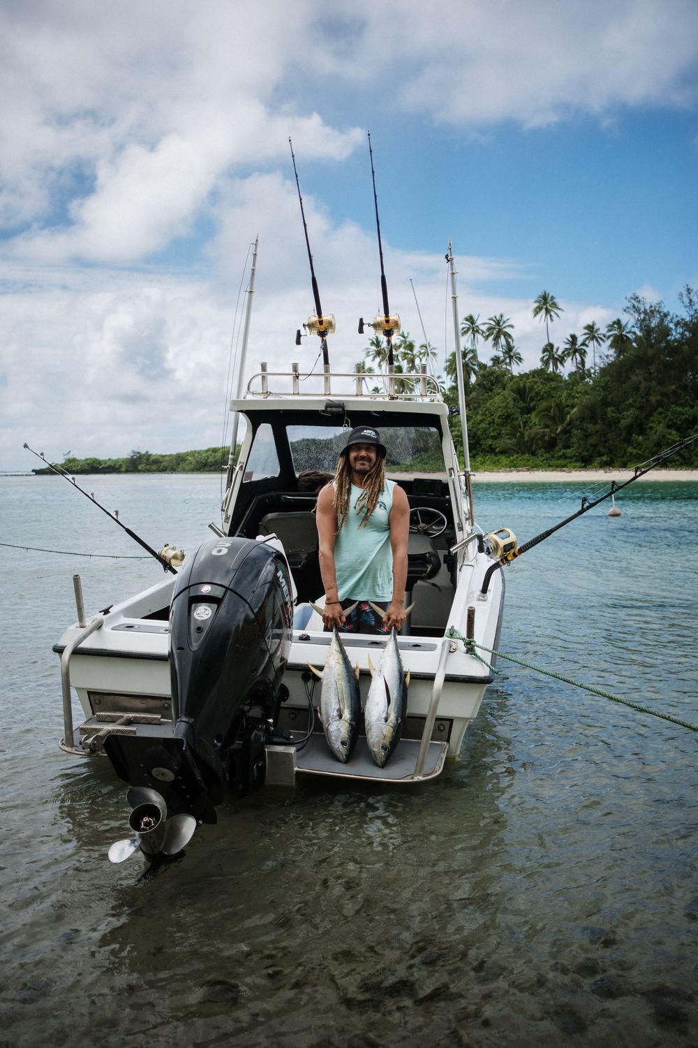 Person enjoying a day of fishing on a small boat near a tropical shoreline with palm trees under blue skies.
