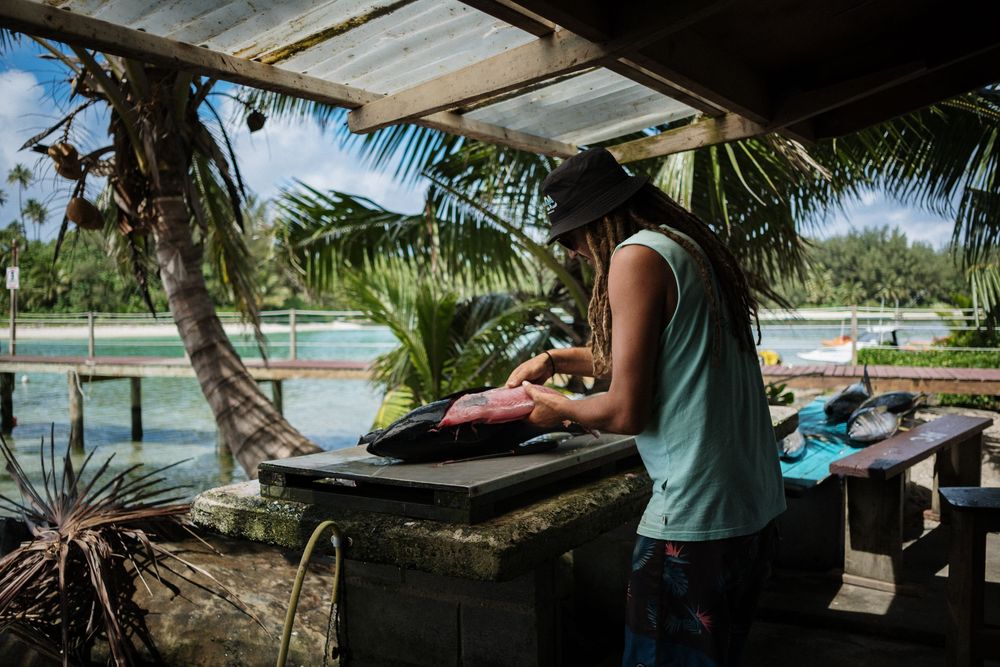 Someone grilling food at an outdoor tropical location with palm trees and water views in the background.
