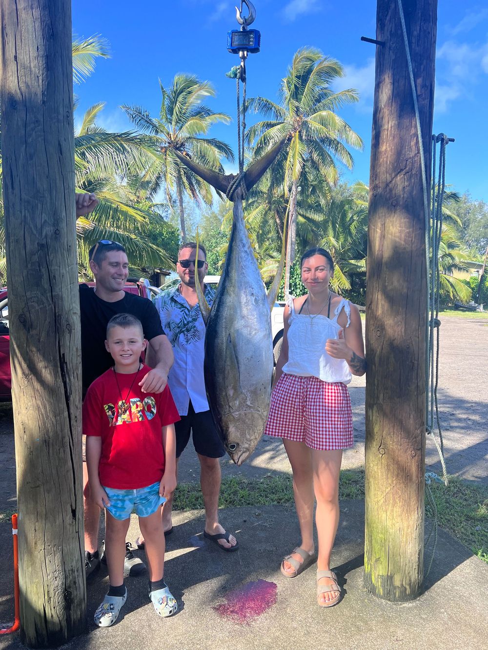 Group displays their catch of large fish hanging from wooden posts at a tropical beach location.