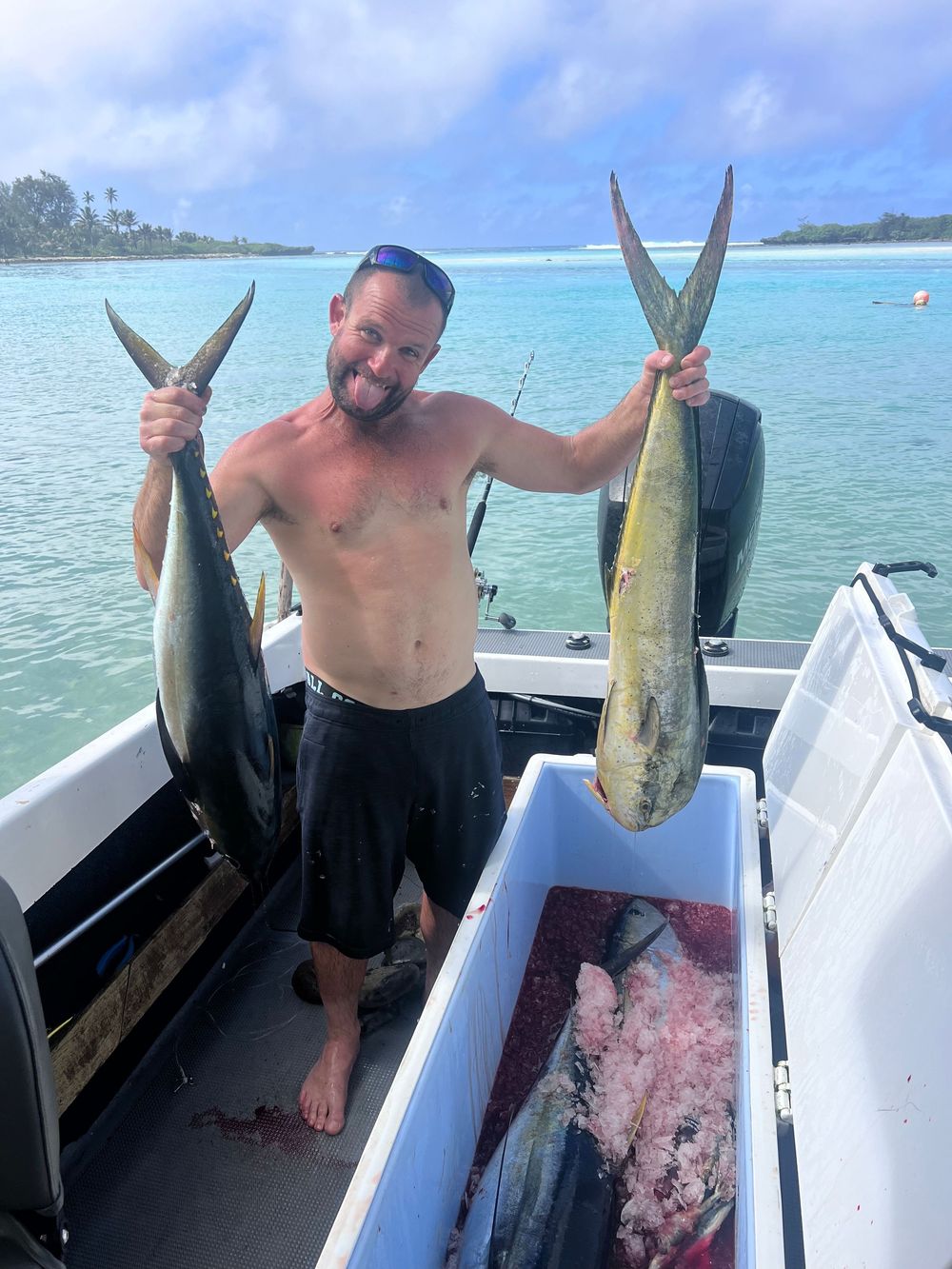 Several mahi-mahi and tuna fish catches displayed on a fishing boat with turquoise waters behind.
