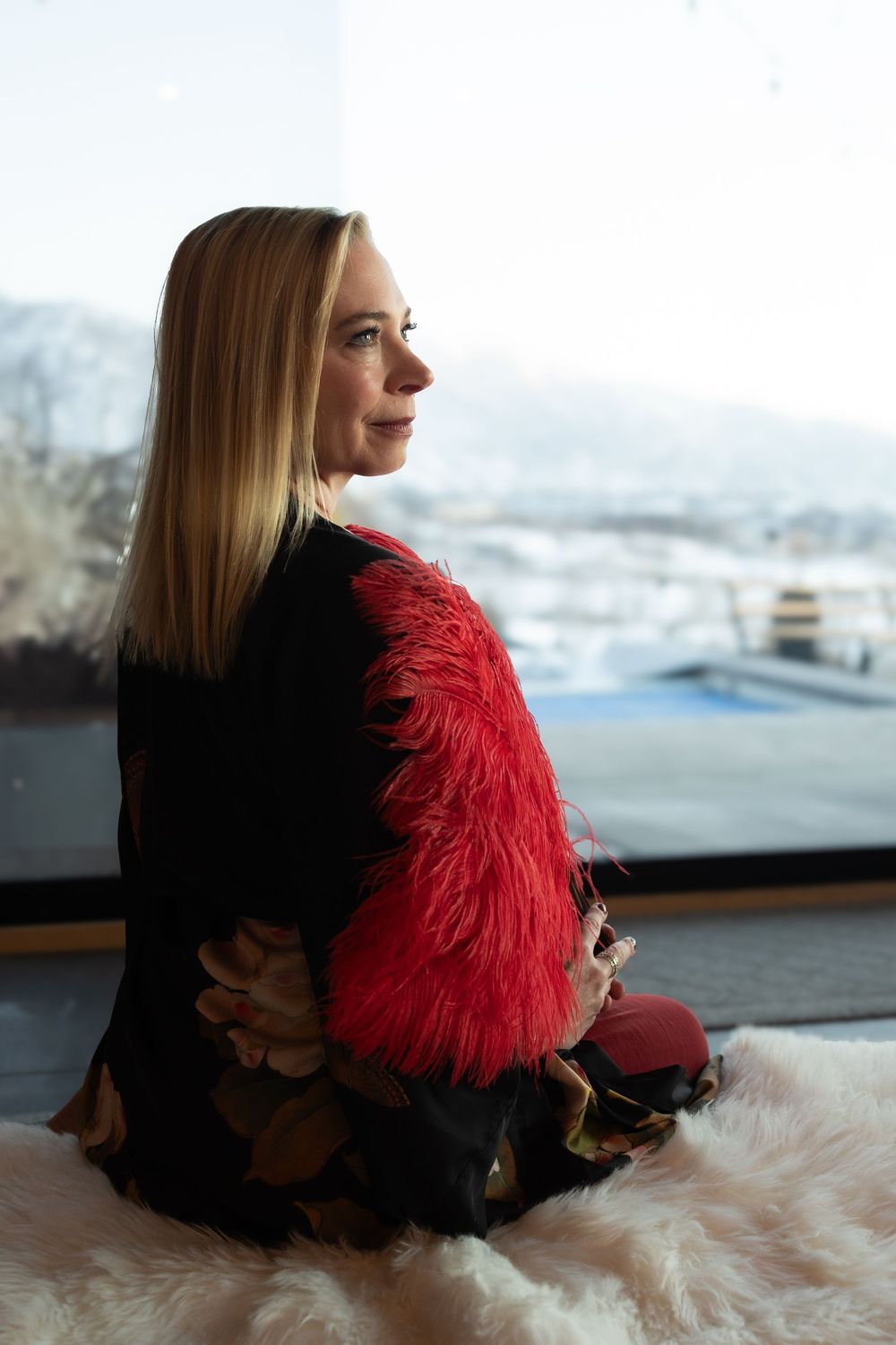 Erica from sensual salon poses by a window with feather fan during event photography session in Salt Lake City.