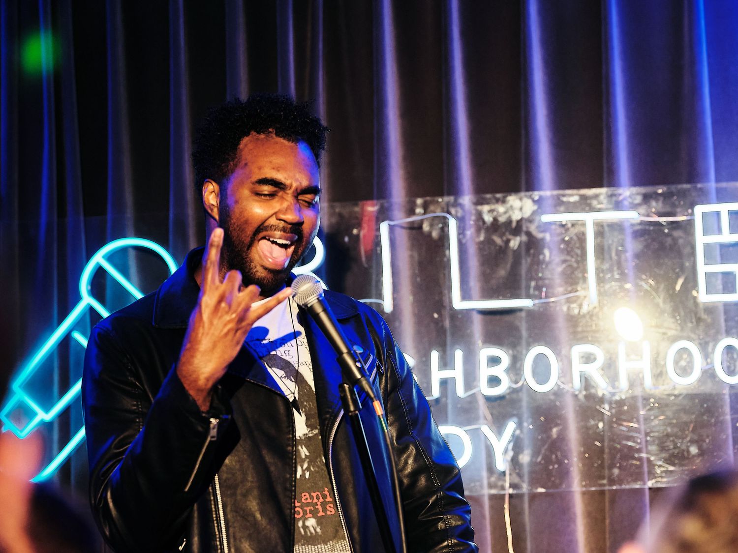 Energetic comedian doing rock-on sign on stage at Bilt Comedy Show at Capo Deli, Washington DC.