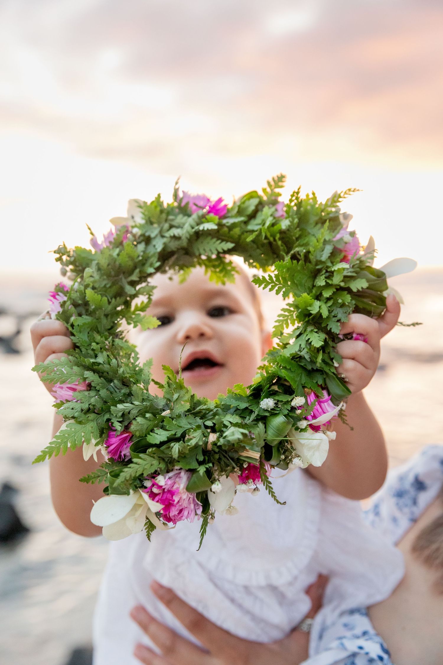 Small floral wreath made of green foliage and pink flowers held up against sunset sky.