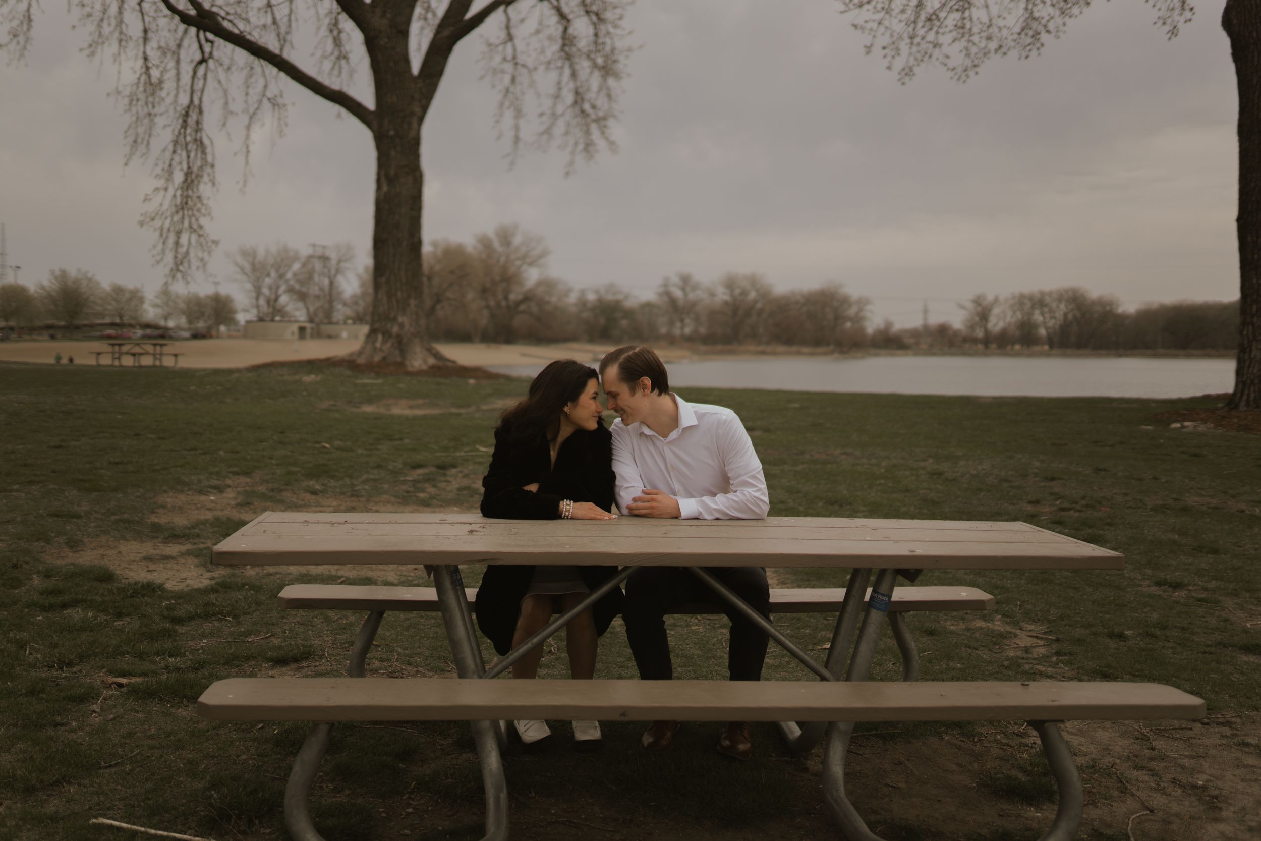 A couple sits together at a rustic wooden picnic table in a moody outdoor setting.