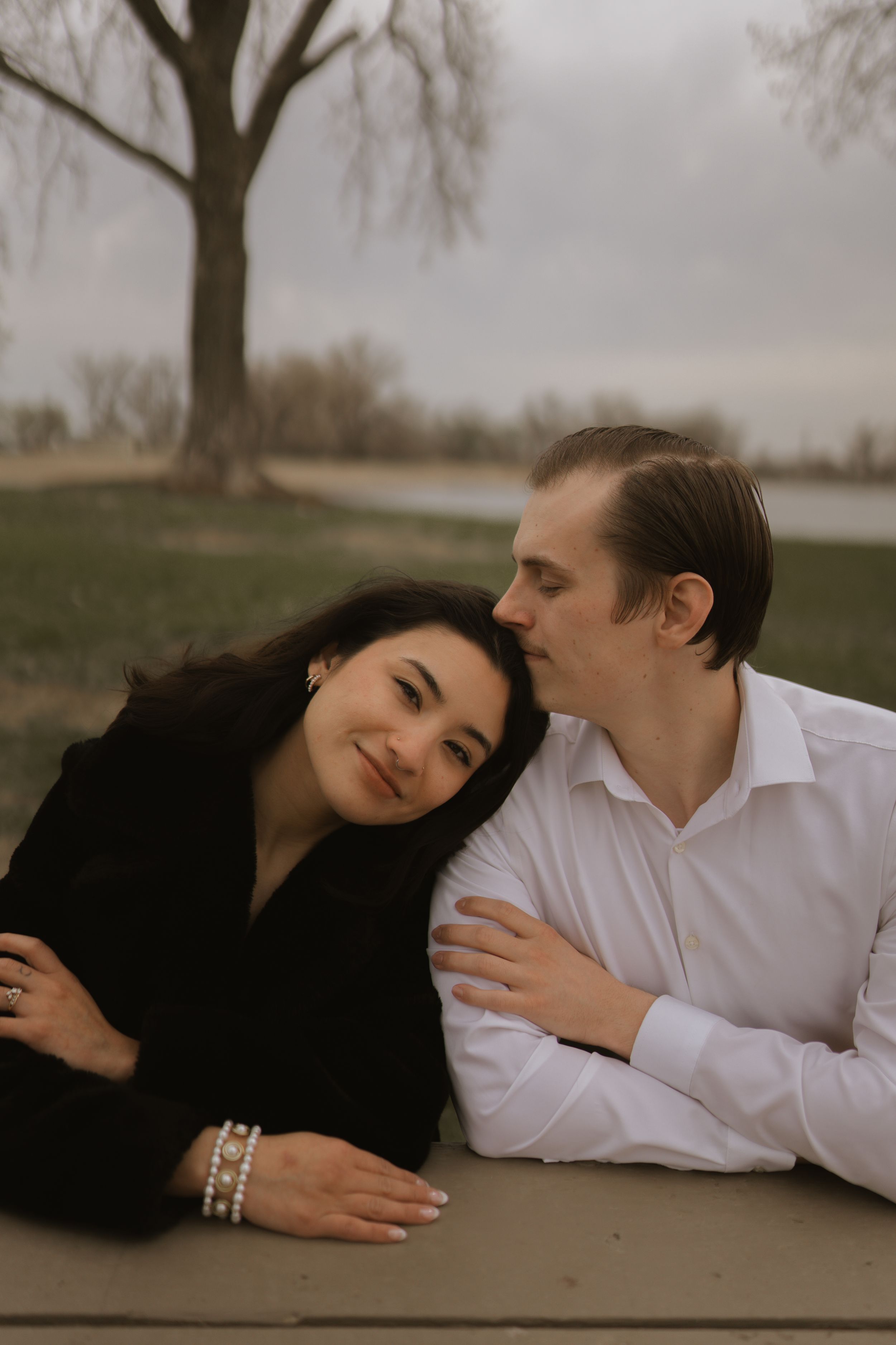 Two people in contrasting black and white outfits lay intimately on a wooden surface outdoors.