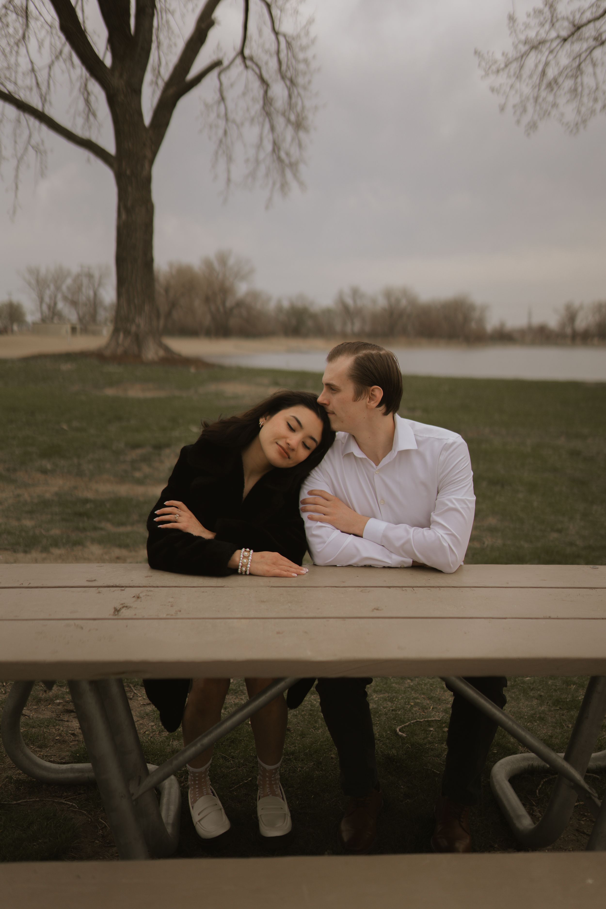 Couple relaxing together on wooden picnic table in park setting.