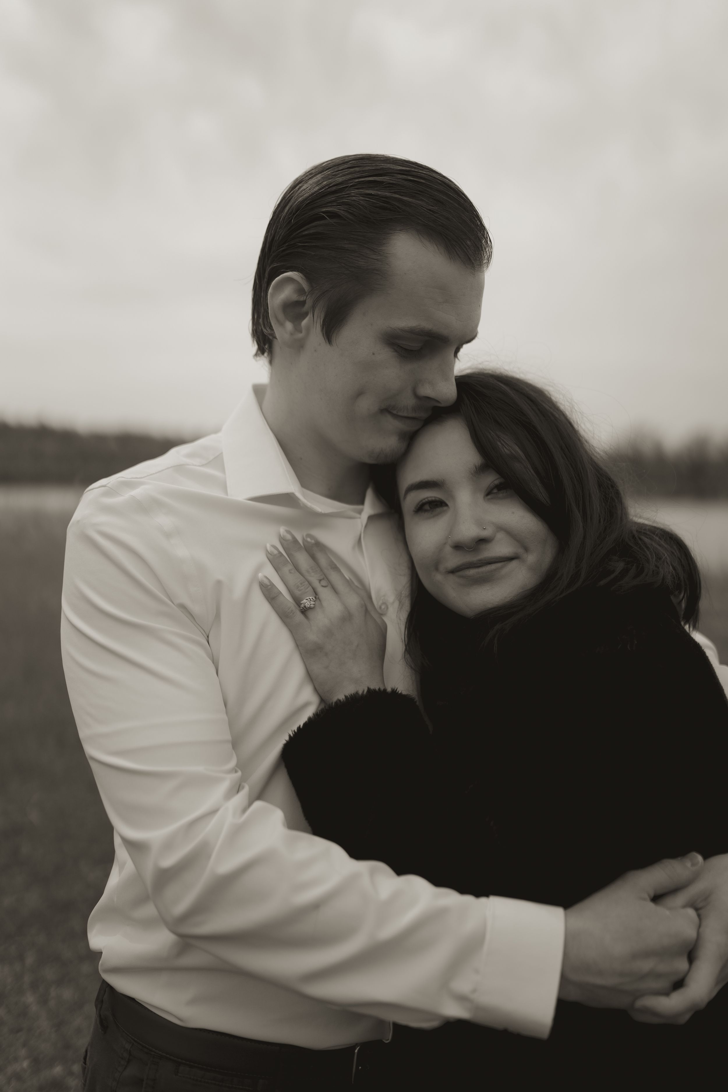 An intimate black and white portrait of a couple embracing outdoors.