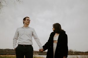 A couple in contrasting outfits stands together in a minimalist outdoor setting.