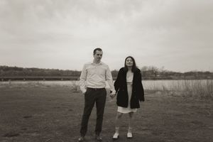 A couple walks hand in hand across an open field under cloudy skies.