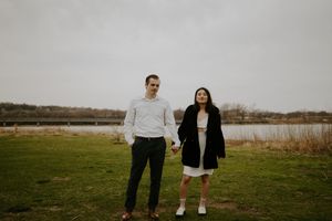 A couple stands together in a scenic outdoor field during golden hour.