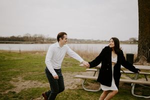 A couple relaxes together near a picnic table by a lake.