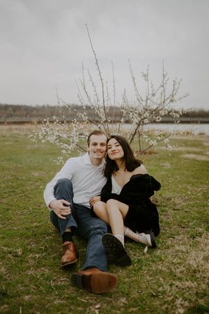 Couple lounges together on grass near blooming spring branches.