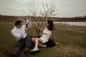 Couple sits beneath flowering tree branches in a natural setting.