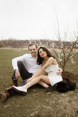 A romantic couple lounges on grass near blooming spring branches during an outdoor photo session.