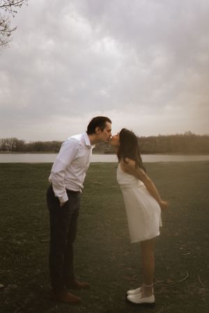 A couple shares a playful moment while posing in a moody field at dusk.