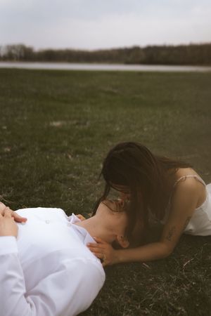 A couple shares an intimate moment while lying on grass during a photo session.