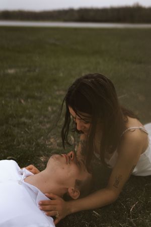 A romantic couple embraces while lying on grass during an outdoor photoshoot.
