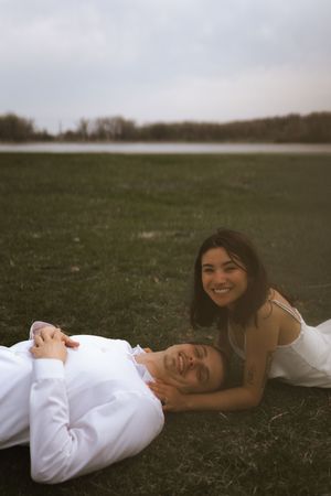 A couple relaxes and smiles while lying on grass during their engagement session.