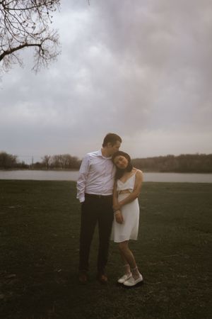 A couple shares an intimate moment in white clothing against a moody sky and lake backdrop.