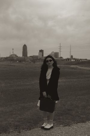 A stylish figure in sunglasses and black coat stands against a city skyline backdrop.
