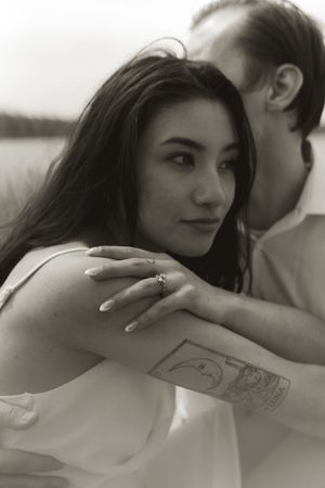 Intimate black and white portrait showing a tattoo on an arm with a lake in the background.