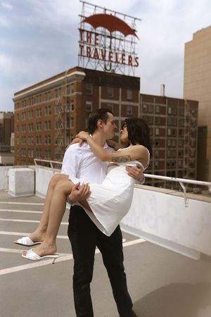 A romantic moment on a rooftop with the iconic Travelers Insurance sign in the background.