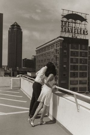 A romantic moment captured in black and white on a city rooftop with urban architecture in view.